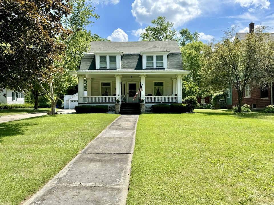 White two-story house with lap siding, front porch and a long green lawn