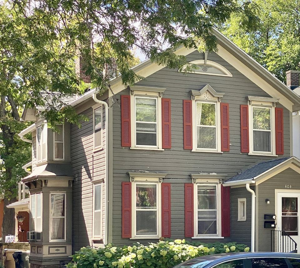 Gray lap-sided two-story house with red window shutters and white trim
