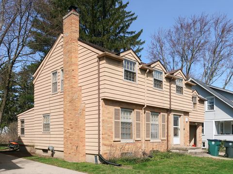 Two-story colonial house with tan lap siding, shuttered windows and brick chimney