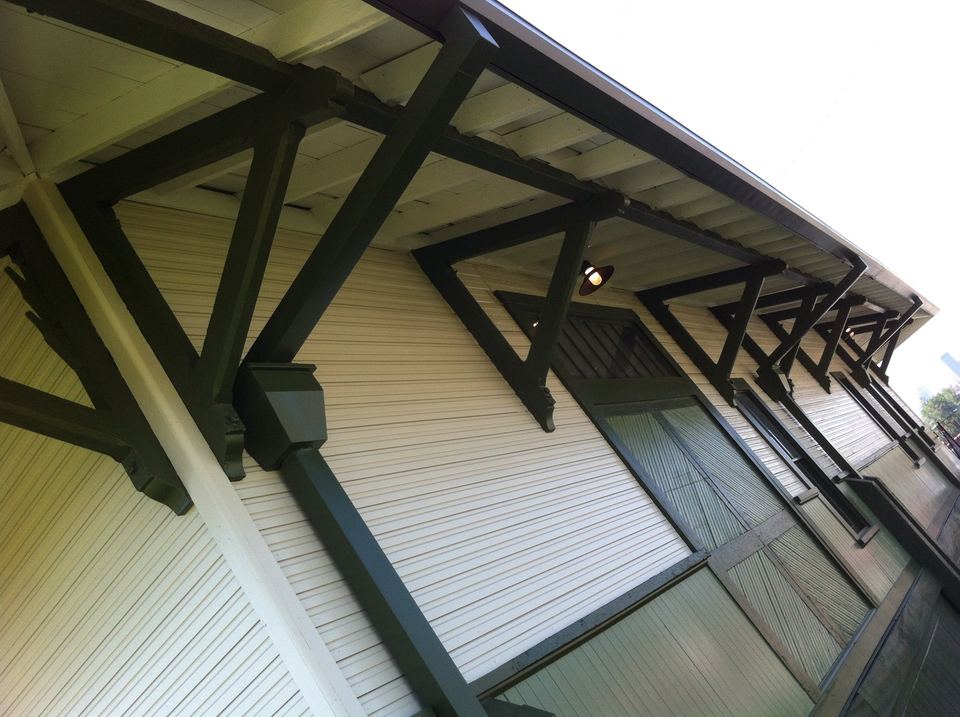 Dark painted eave brackets and soffit above white vinyl siding and windows