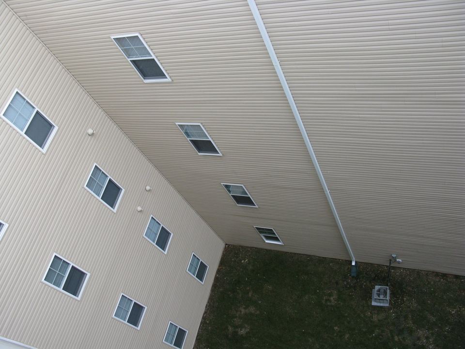 Looking up a tall wall of beige vinyl siding with small white windows
