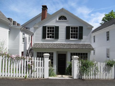 White clapboard house with black-shuttered double-hung windows behind a white picket fence